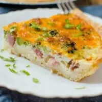 A slice of ham and broccoli quiche served on a white plate.