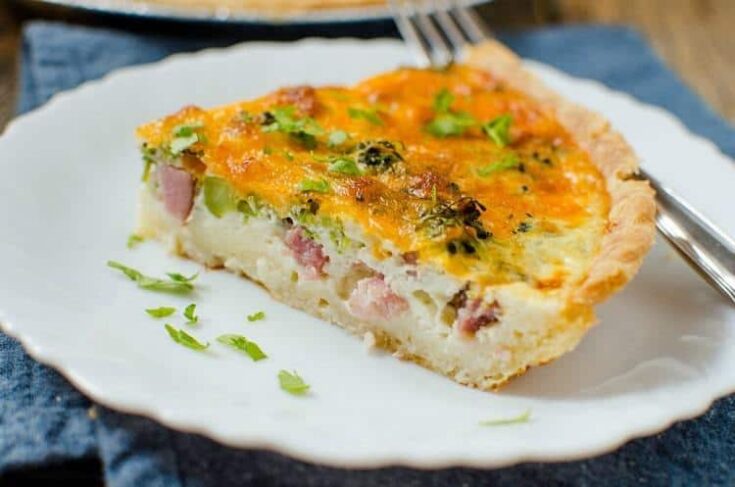 A slice of ham and broccoli quiche served on a white plate.