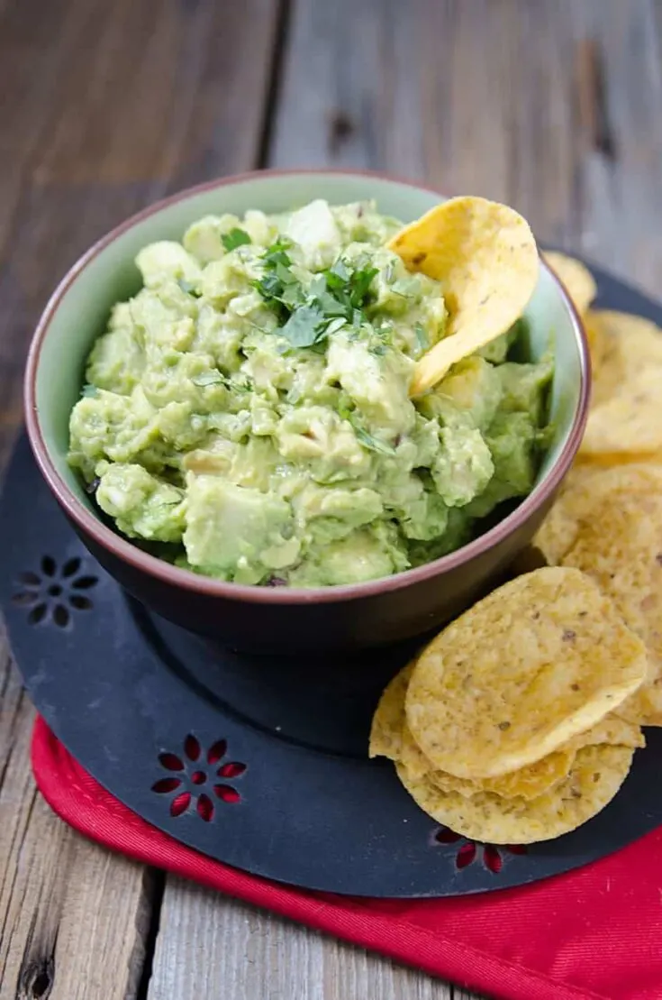Homemade guacamole on a bowl with some tacos beside it.