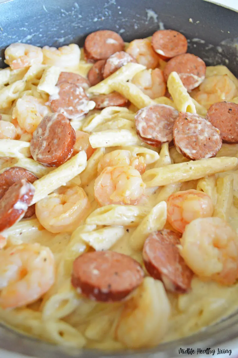 pasta and shrimp being added to the sauce. 