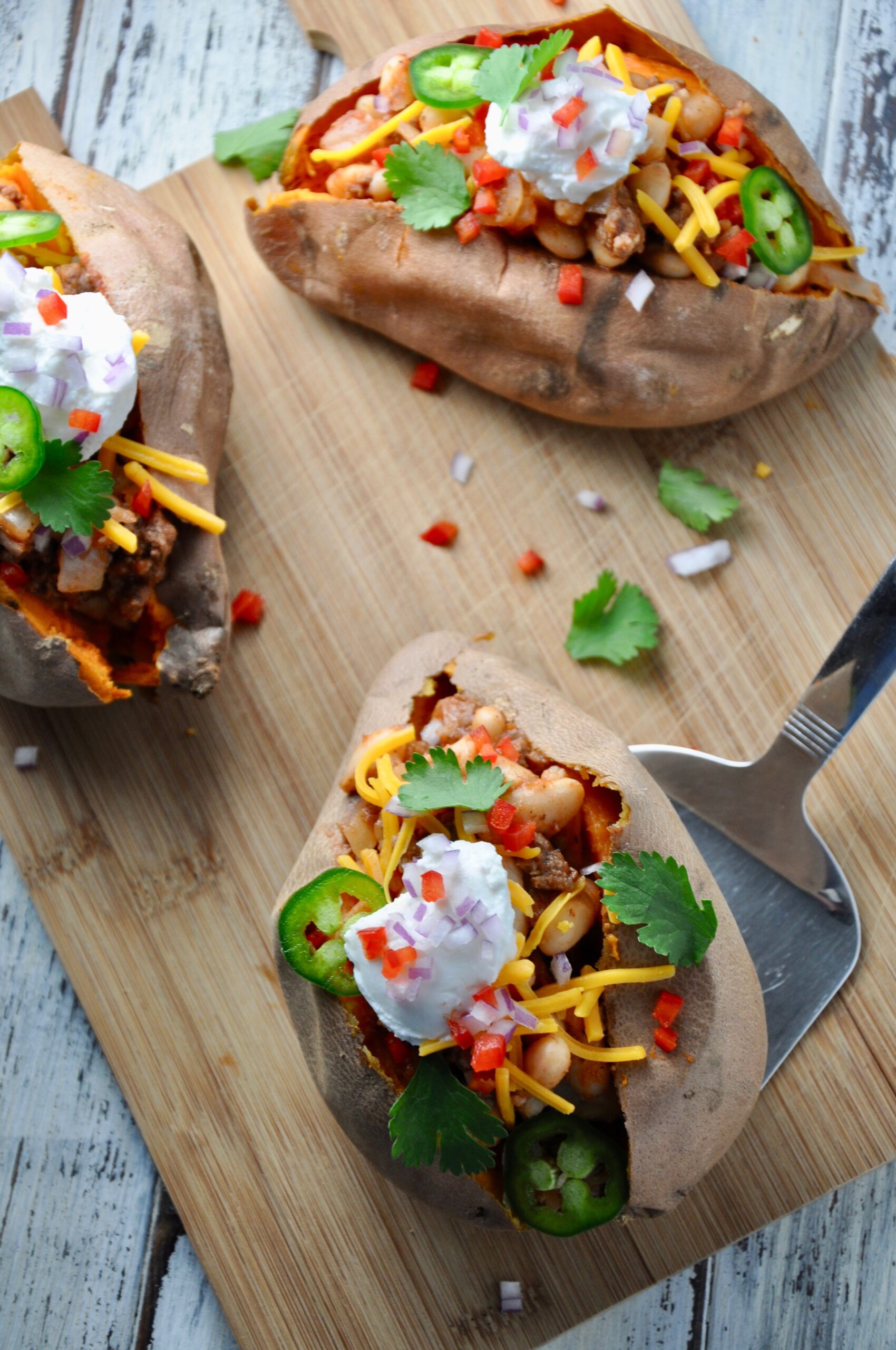 baked potatoes stuffed with chili tipped with cheese, jalapenos and sourcream on a cutting board