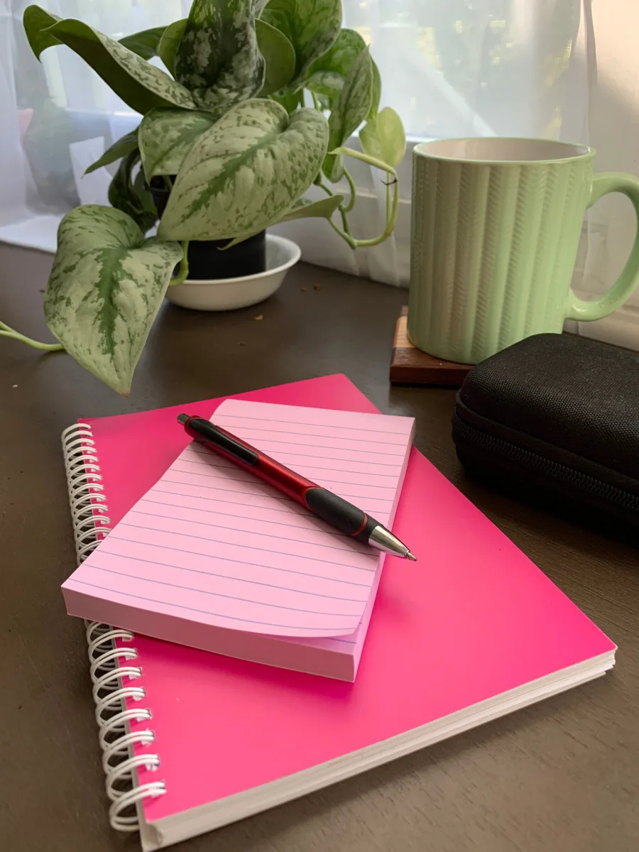 pink note book and pink note pad with a red pen on top