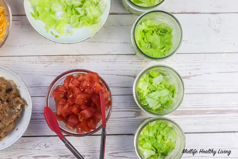 Adding in the tomatoes to the lettuce in the jars