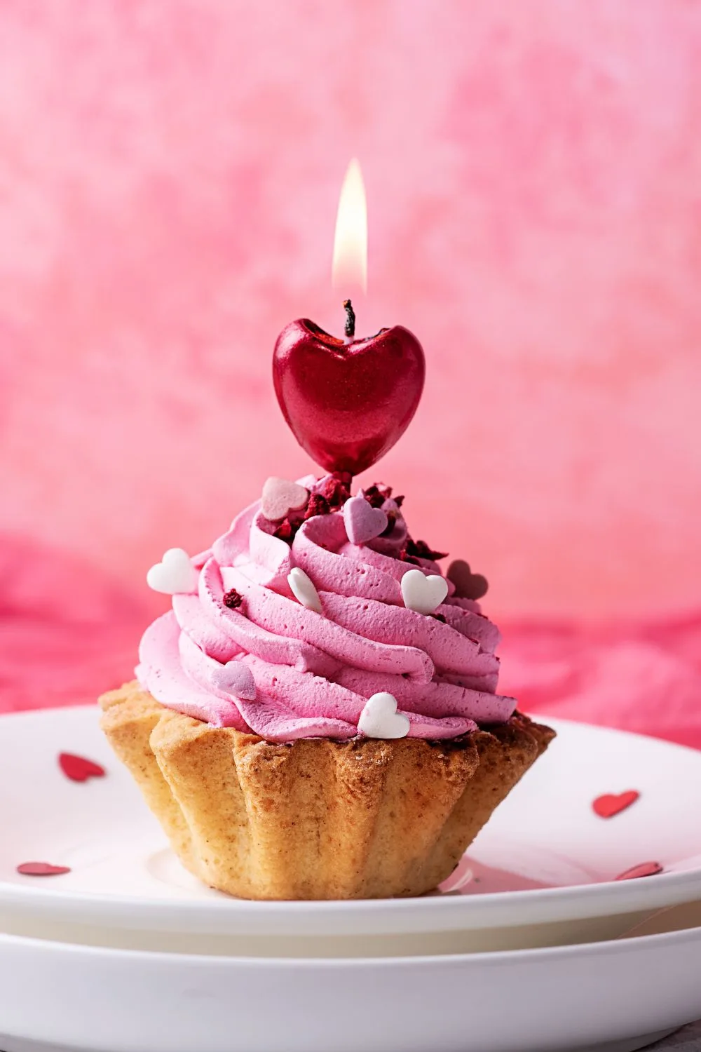 A Valentine's Day themed tart with pink frosting. There is a lit heart shaped candle on top.