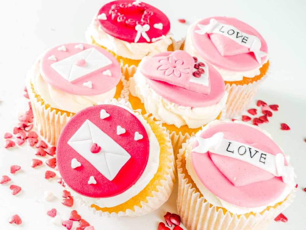Vanilla cupcakes with various Valentine's Day themed decorations on top in various shades of pink.