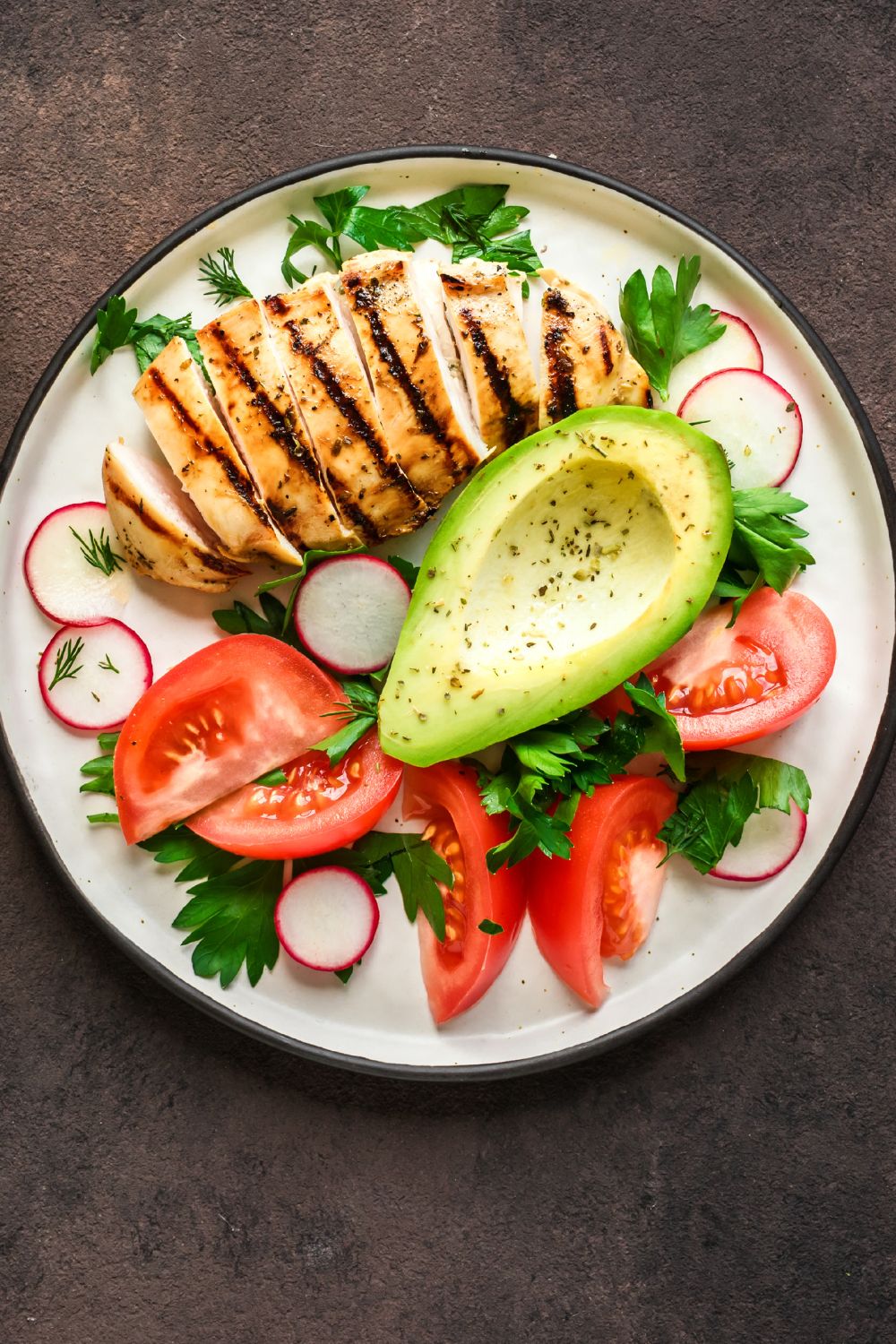 A plate filled with healthy foods such as chicken, avocado, and vegetables