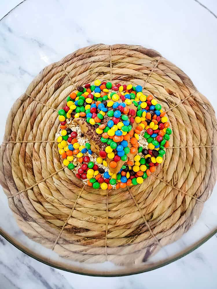 Overhead view of oats, peanut butter, flax seeds, and m&ms in a clear mixing bowl.