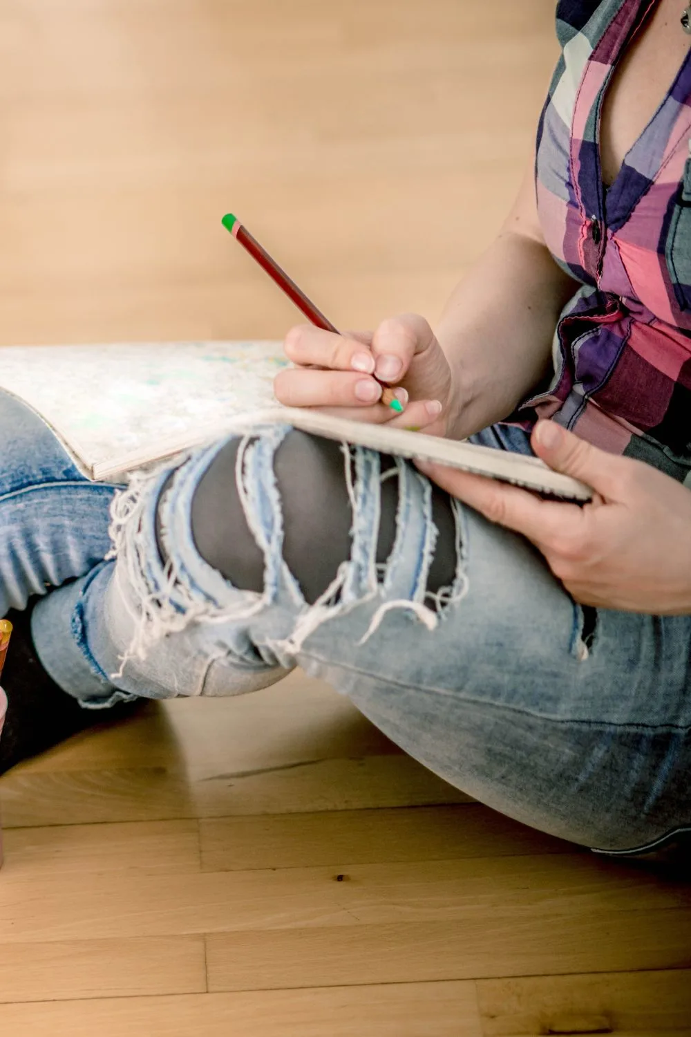 Someone sitting on the floor coloring with a green pencil crayon