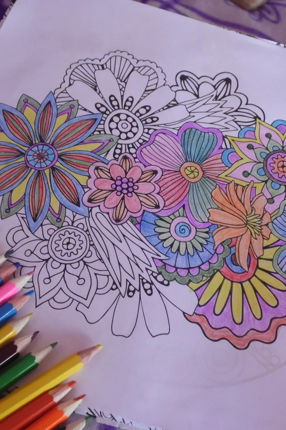 a floral coloring page partially colored in by the surrounding pencil crayones