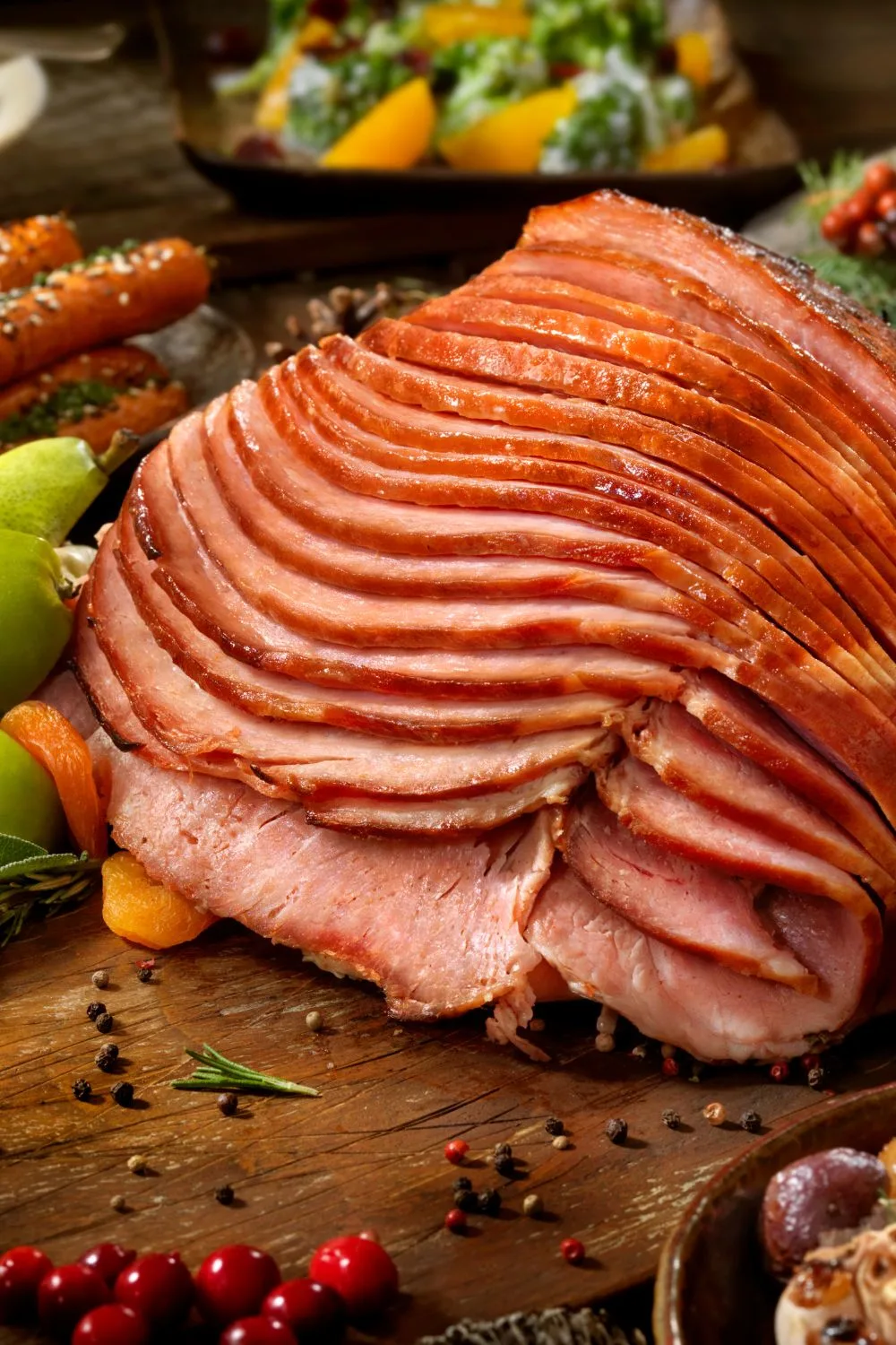 a baked ham sliced up with vegetables in the background