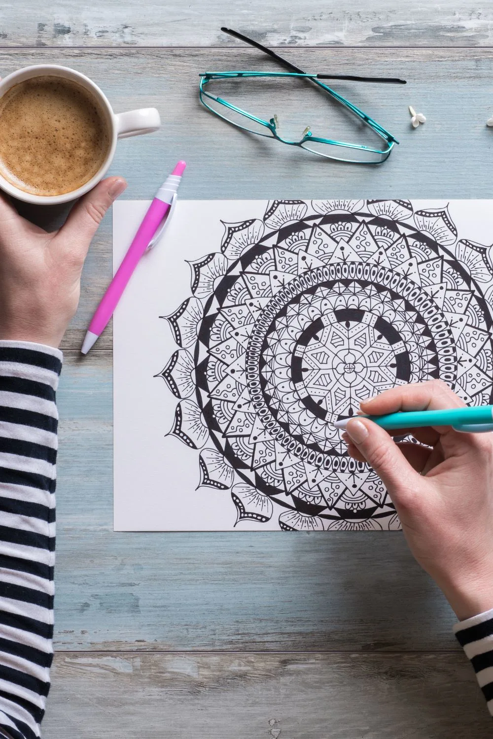 person coloring in a mandala coloring page with a coffee in their hand