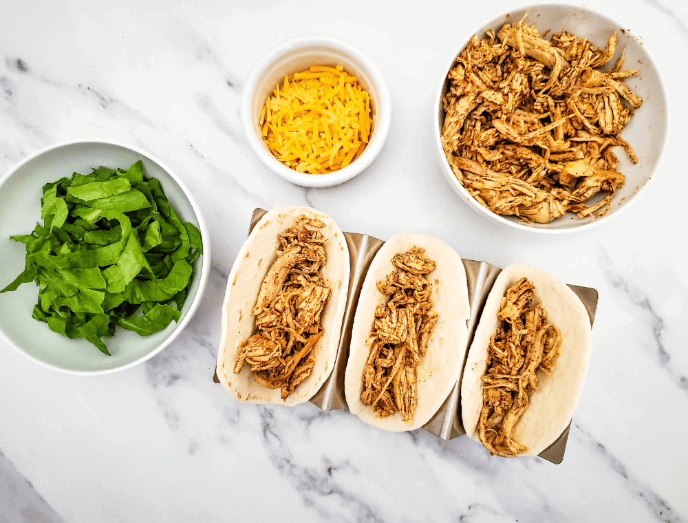 adding shredded chicken to tortilla shells for chicken street taco