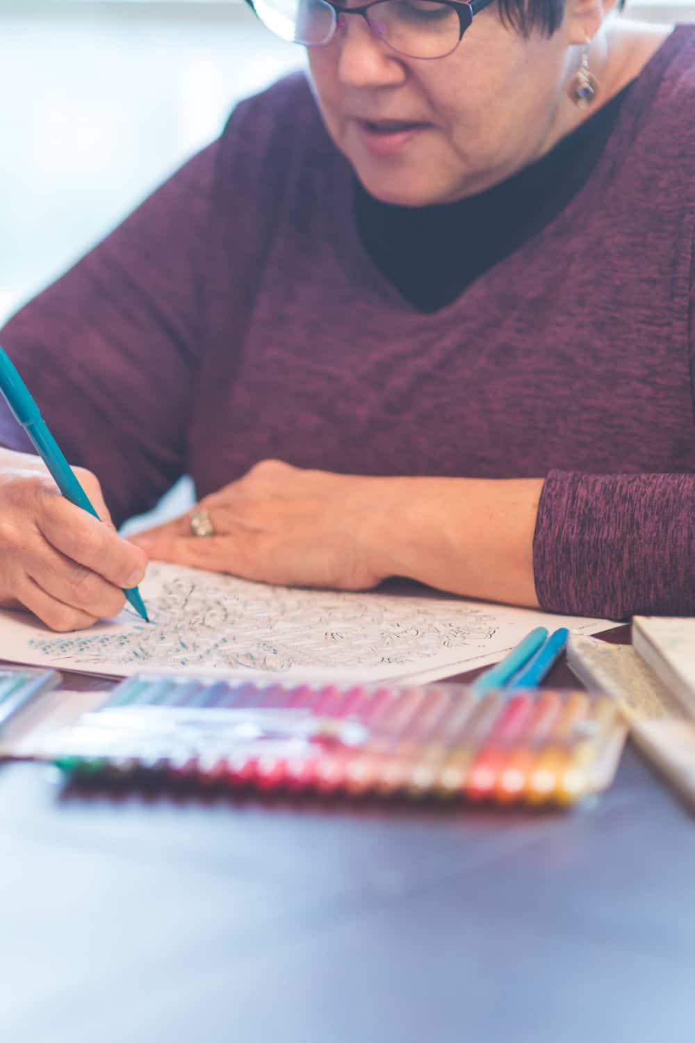 A woman sitting at a table coloring in a printable coloring page for adults