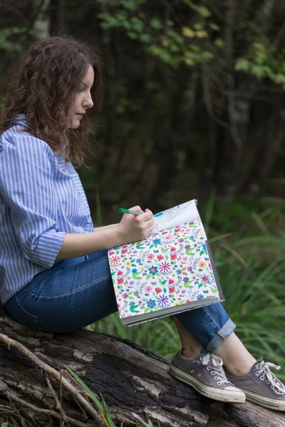 a woman sitting outside coloring in a coloring book