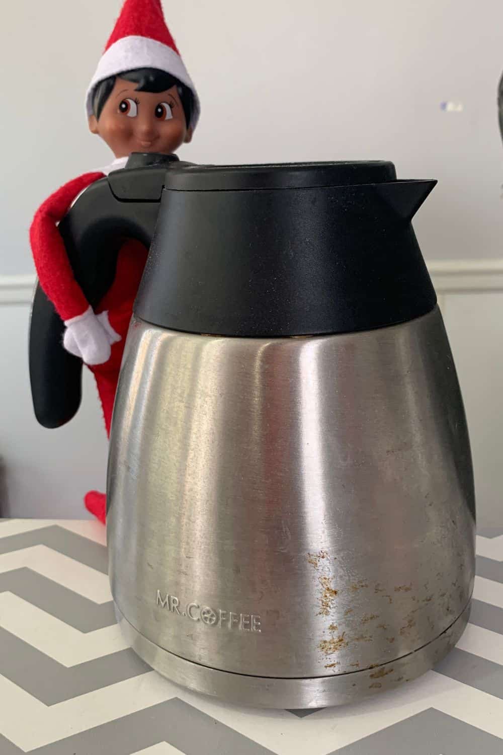 an Elf on the Shelf hanging onto a coffee pot