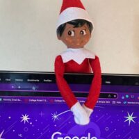 Elf on the Shelf hanging onto the back of a laptop computer