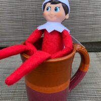 Elf on the shelf sitting on a coffee mug