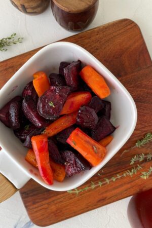 a white bowl filled with roasted carrots and beets on a wooden cutting board