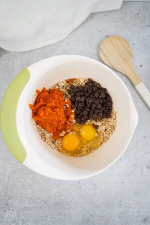 adding eggs, chocolate chips, and pumpkin puree to the mixing bowl