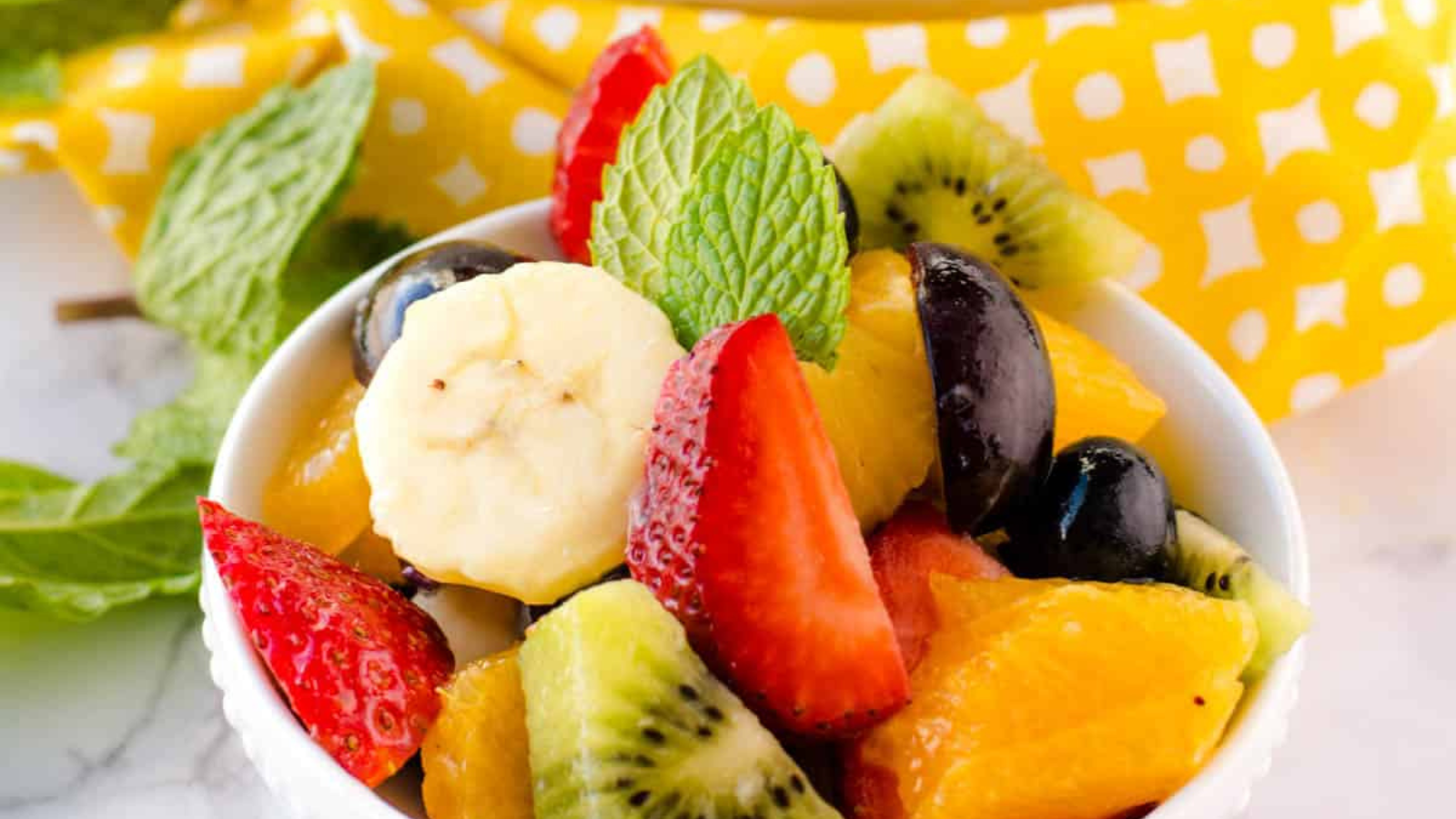 A bowl of fruit salad with honey lime sauce.