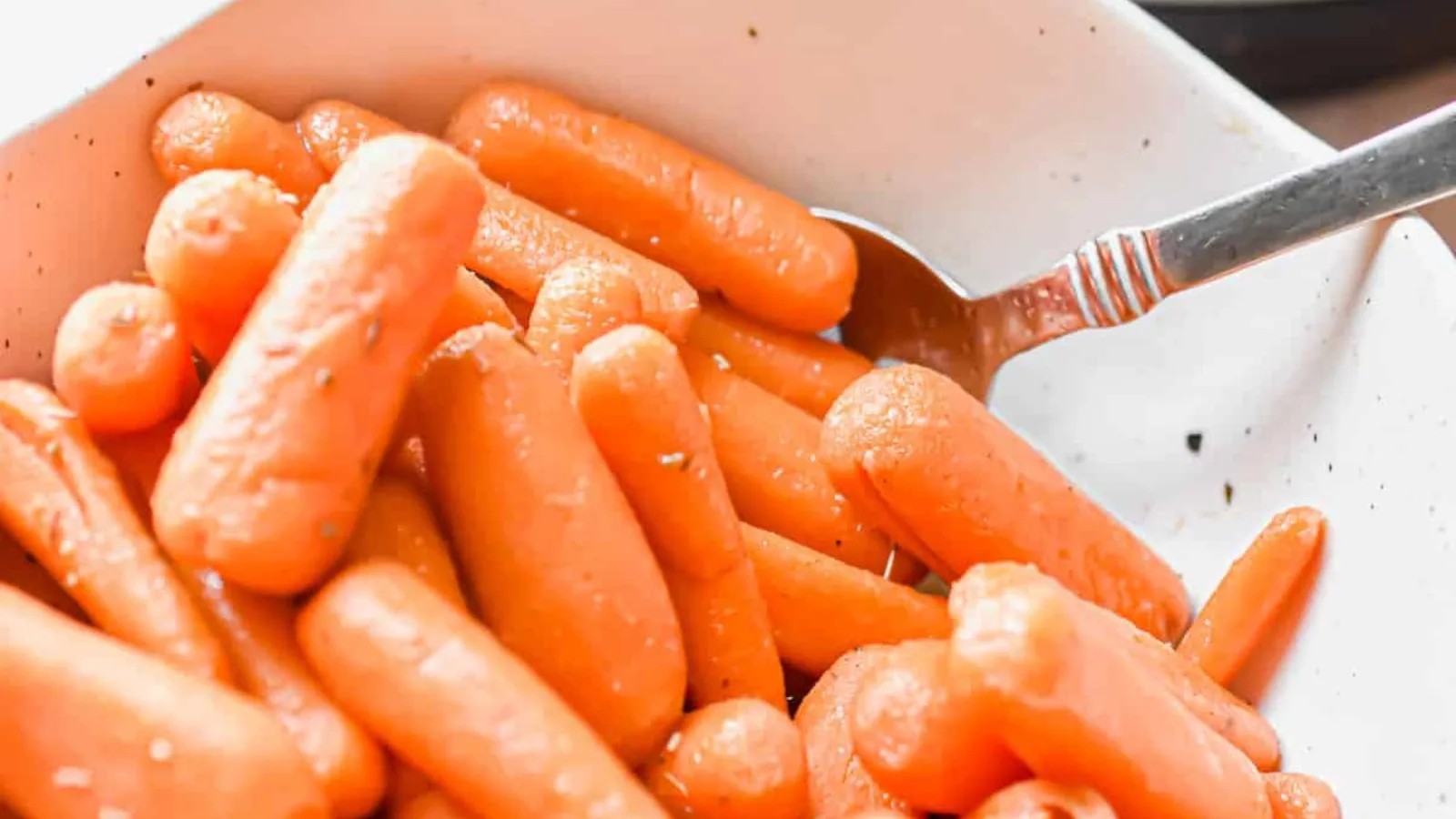 A bowl of baby carrots with a spoon.