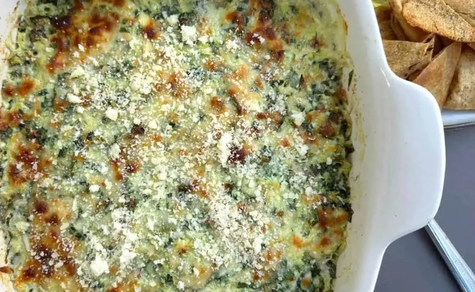 A casserole filled with spinach crab artichoke dip with cheese and tortilla chips.