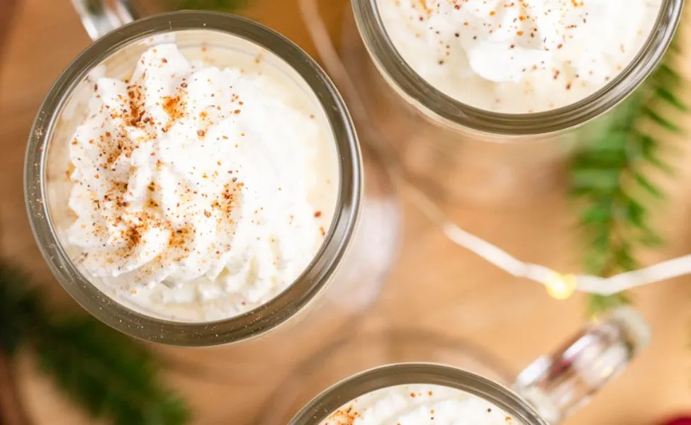 Tall mugs of keto eggnog with whipped topping.