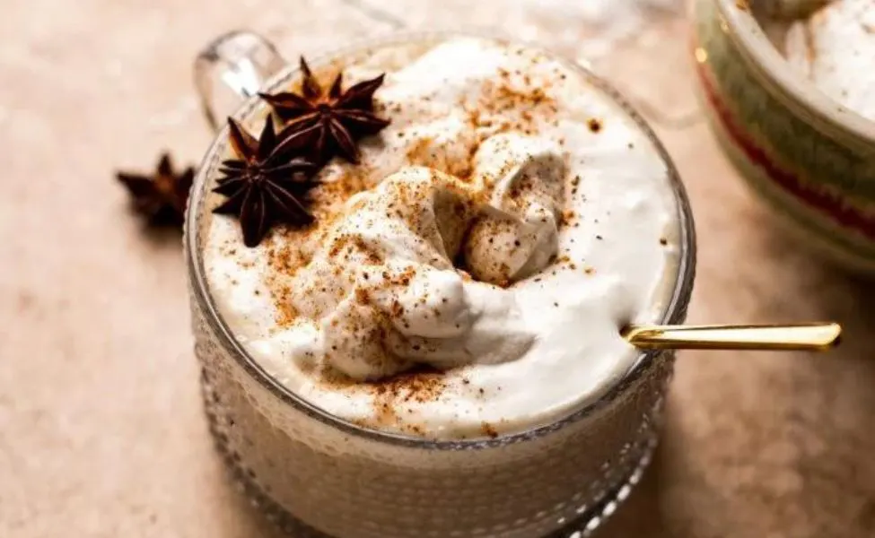 A wide mug with creamy eggnog with star anise on top.