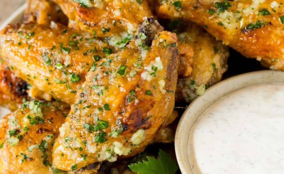 A tray of wings with herb coating and a bowl of dip nearby.